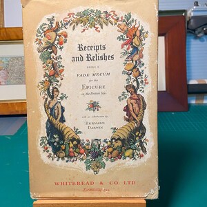 May include: A vintage book cover with the title "Receipts and Relishes Being a Vade Mecum for the Epicure in the British Isles." The cover features a colourful illustration of a cornucopia overflowing with fruits, vegetables, and other foods. The book was published by Whitbread & Co. Ltd. and established in 1742.