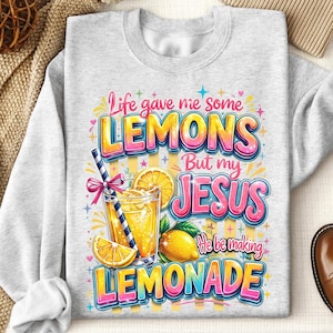 K&ouml;nnte beinhalten: Hellgraues Sweatshirt mit farbenfroher Grafik. Die Grafik zeigt den Text "Life gave me some LEMONS But my JESUS He be making LEMONADE" mit einem Glas Limonade, Zitronenscheiben und einer ganzen Zitrone.