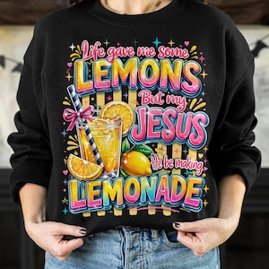 K&ouml;nnte beinhalten: Schwarzes Sweatshirt mit einem farbenfrohen Aufdruck: "Life gave me some lemons but my Jesus he be making lemonade." Das Design zeigt ein Glas Limonade, Zitronenscheiben und eine ganze Zitrone.