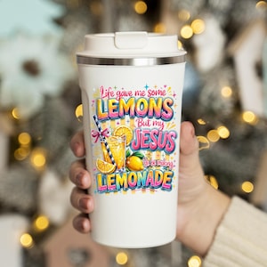 K&ouml;nnte beinhalten: Wei&szlig;er Reisebecher mit silbernem Deckel, mit dem Text "Life gave me some LEMONS But my JESUS He be making LEMONADE" in bunten Buchstaben. Das Design beinhaltet eine Grafik von Limonade und Zitronen.
