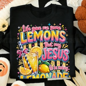 K&ouml;nnte beinhalten: Schwarzes Sweatshirt mit einem farbenfrohen Grafikdesign. Das Design zeigt den Text "Life gave me some LEMONS But my JESUS He be making LEMONADE" mit einem Glas Limonade und Zitronen.
