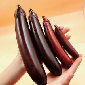 May include: Four wooden eggplant sculptures in varying sizes and shades of brown and red. The sculptures are held in a person's hands, showcasing the detailed craftsmanship and natural wood grain.