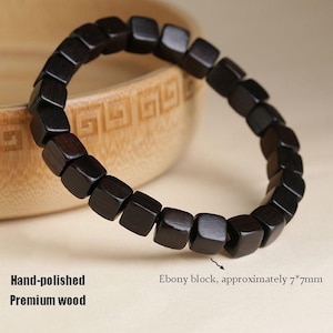 Könnte beinhalten: Ein dunkelbraunes, handpoliertes Holzarmband. Das Armband besteht aus quadratischen Ebenholzblöcken, die jeweils etwa 7 mm groß sind. Der Text auf dem Bild lautet "Hand-polished, Premium wood."