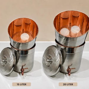 May include: Two cylindrical water dispensers made of stainless steel with copper-coloured interiors. Each unit features a metal lid, a spigot at the base, and a white filter element inside. Labels indicate capacities of 15 litres and 20 litres respectively.