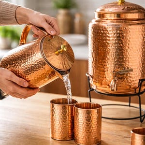 Może przedstawiać: Biały ceramiczny kubek z czarnym uchwytem i napisem "But First, Coffee" czarną, pogrubioną czcionką. Kubek stoi na białej powierzchni. Kubek ma około 10 cm wysokości.