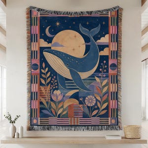May include: A woven throw blanket featuring a large blue whale centered against a golden moon and a dark blue night sky with stars and a crescent moon. The design includes stylized floral elements, geometric patterns, and a fringed edge border.