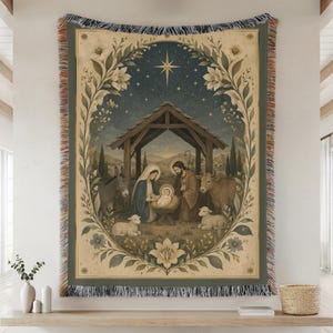 May include: A woven tapestry blanket featuring a nativity scene with a central manger, figures of Mary and Joseph, a donkey, a cow, and two lambs. The scene is framed by a floral border with a star above, all set against a dark blue night sky.