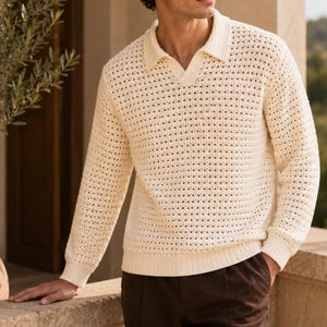 May include: A cream-colored long-sleeve polo sweater featuring an open-knit, textured pattern throughout the body and sleeves. The garment includes a classic collar, a V-neck placket, and solid ribbed cuffs and hem for a structured finish.