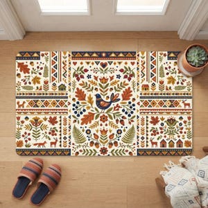 Puede incluir: Un felpudo rectangular con fondo crema y un patrón repetitivo de arte popular. El diseño incluye un pájaro central, flores estilizadas, hojas de roble, helechos, bellotas, bayas, casas pequeñas, zorros y ciervos en tonos naranja, azul y verde.