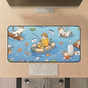 May include: A rectangular mousepad featuring a whimsical illustration of cats fishing in a blue pond. One cat in a yellow raincoat fishes from a boat, surrounded by orange fish and other cats. A keyboard, mouse, and computer are visible.