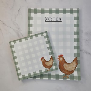 May include: Two rectangular paper notepads featuring a sage green and white gingham border pattern. The larger notepad has the word NOTES printed in black at the top. Both notepads display a brown chicken illustration in the bottom corner.