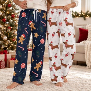 May include: Two pairs of lounge pants with elastic waistbands and white drawstrings. One pair is dark blue with gingerbread men, candy canes, lollipops, and pine branches. The other pair is white with dachshunds wearing Santa hats and scarves.