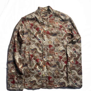 May include: A long-sleeved button-down shirt featuring a dense, intricate paisley pattern in shades of beige, brown, red, and blue. The shirt has a mandarin collar and a front placket with small, multi-coloured buttons in various hues.