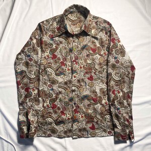 May include: A long-sleeve button-down shirt featuring a dense, multi-coloured paisley pattern in shades of brown, red, blue, and gold on a cream background. The shirt has a pointed collar and a front placket with small, multi-coloured buttons.