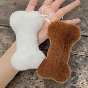 May include: Two fluffy, bone-shaped accessories, one white and one brown. A white USB cable is attached to the white bone. The items are on a wooden surface.
