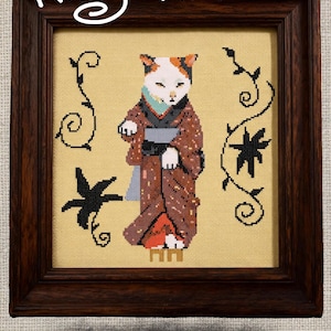 May include: Cross-stitch pattern showing a cat in a kimono. The cat is brown, white, and orange, wearing a brown kimono with black details. The background is yellow with black floral designs. Text reads "Kitty Kimono" and "Cross Stitch Pattern".