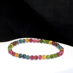 Könnte beinhalten: Ein kreisförmiges Perlenarmband mit kleinen, glatten, runden Edelsteinen in verschiedenen Farben, darunter tiefes Rot, Waldgrün, Goldgelb und Dunkelblau. Die Perlen sind in einem sich wiederholenden Muster zu einer durchgehenden Schlaufe aufgereiht.