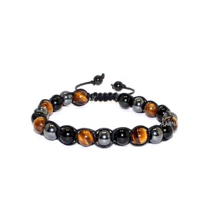 May include: A beaded bracelet featuring alternating round tiger eye, black onyx, and metallic hematite beads strung on a black cord. The bracelet includes an adjustable macrame sliding knot closure with two small beads at the ends of the pull strings.