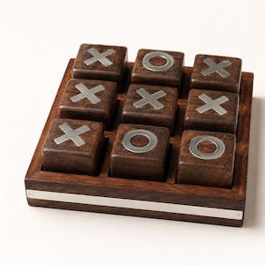 May include: A wooden tic-tac-toe game set featuring a square board with a silver metal strip along the front edge. The game includes nine individual dark brown wooden cubes, each inlaid with a silver metal X or O symbol on the top surface.