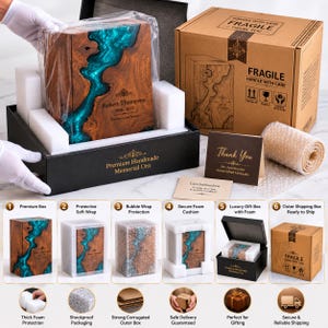 May include: A rectangular wooden memorial urn featuring a vibrant turquoise resin river inlay. The front is engraved with the name Robert Thompson, the dates 1948-2023, and the text Forever in our hearts. It is packaged in a black box with foam.