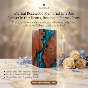 May include: A rectangular rosewood memorial urn box featuring a central river-like inlay of translucent teal resin. The front is engraved with the text Robert Thompson 1948-2023. The urn is displayed alongside a lit candle and cream-colored roses.