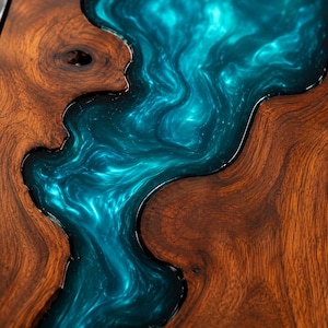 May include: A live edge wood slab table surface featuring a central river design made of swirling, metallic turquoise epoxy resin. The natural brown wood grain displays organic knots and patterns bordering the glossy, fluid-like blue resin inlay.