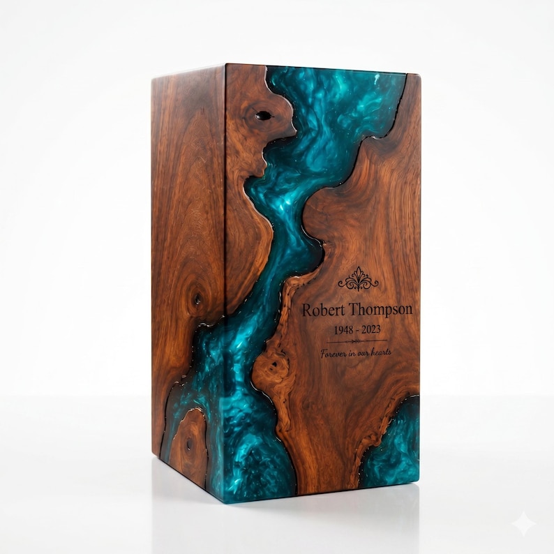 May include: A rectangular wooden cremation urn featuring a natural dark brown wood grain and a central flowing inlay of translucent teal blue resin. The front surface is engraved with the text Robert Thompson, 1948-2023, and Forever in our hearts.