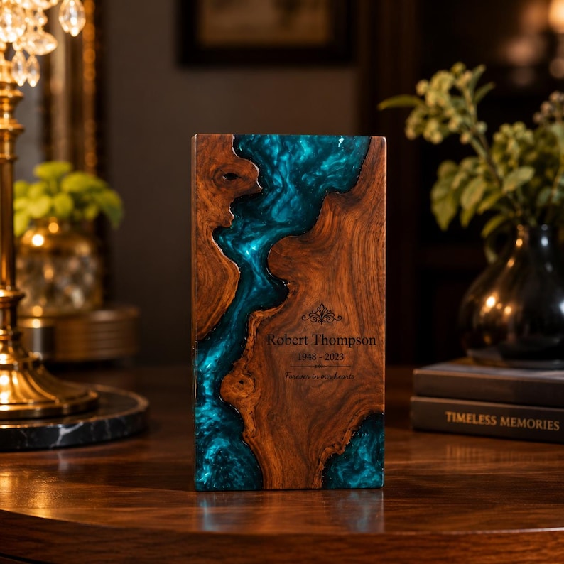May include: A rectangular wooden memorial plaque featuring a central river-like inlay of swirling teal resin. The wood has a natural grain and live edge. Engraved text reads: Robert Thompson, 1948-2023, Forever in my hearts.