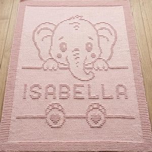 Puede incluir: Una manta rectangular de punto color rosa claro que presenta un diseño de elefante texturizado en la parte superior, el nombre ISABELLA en letras mayúsculas en el centro y dos corazones pequeños en la parte inferior, con un borde ancho.
