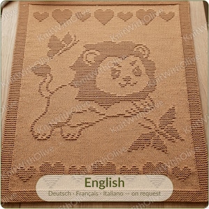 Puede incluir: Una manta de punto rectangular de color tostado con un diseño de león texturizado en el centro, rodeado por un borde de pequeños corazones tejidos. Una libélula se encuentra cerca de las patas del león. El texto English, Deutsch, Français, Italiano - on request está impreso en la parte inferior.