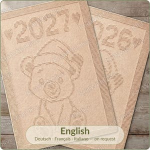 May include: Two rectangular beige knit blankets featuring a textured design of a teddy bear wearing a hat. The primary blanket displays the year 2027 flanked by two hearts, while the partially visible second blanket shows the year 2026.