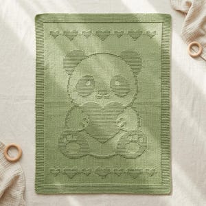 May include: A sage green knitted baby blanket featuring a panda bear holding a heart. The blanket has a border of hearts along the top and bottom edges. The soft blanket is made of a textured knit.