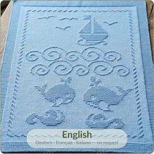 Puede incluir: Una manta de punto azul claro con un diseño náutico texturizado que muestra un velero, olas estilizadas y dos ballenas. El borde tiene un patrón de puntada decorativo. El texto "English Deutsch Français Italiano - on request" es visible.