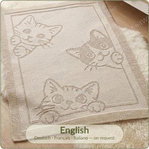 May include: A rectangular beige knit blanket featuring a textured border and three cat faces peeking from the edges. The design includes the repeated watermark text KnitWithOlive across the surface. The blanket has a soft, woven appearance.