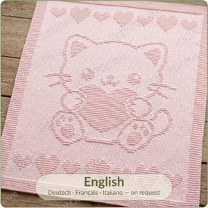 Puede incluir: Una manta tejida de color rosa claro con un diseño central texturizado de un gato sosteniendo un corazón. El borde está enmarcado por una fila de pequeños corazones tejidos en los bordes superior e inferior. El texto KnitWithOlive es visible.