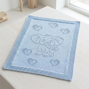 May include: A light blue rectangular knitted blanket featuring a central elephant motif surrounded by five stylized heart shapes. The blanket has a textured garter stitch border framing the smooth stockinette stitch center panel with the design.