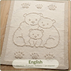 Peut inclure: Une couverture rectangulaire en tricot beige présentant un motif texturé de trois ours et six empreintes de pattes. Le design est réalisé avec des mailles en relief sur un fond en jersey, bordé d'une large bordure côtelée sur les quatre côtés.