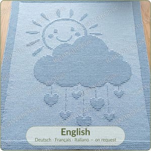 May include: A light blue knitted blanket featuring a textured pattern of a smiling sun partially obscured by a large cloud. Below the cloud, several heart-shaped raindrops are suspended by vertical lines. The border has a ribbed knit edge.