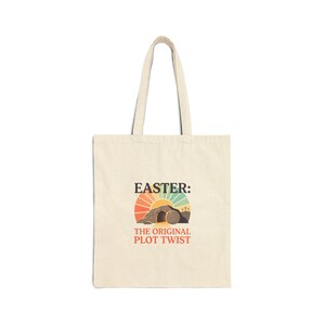 May include: A cream-coloured tote bag featuring the text "EASTER: THE ORIGINAL PLOT TWIST." The graphic shows a sunrise over a tomb with three crosses. The bag has two handles.