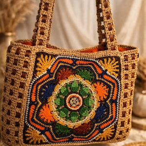 May include: A handcrafted crochet tote bag with a colorful floral design. The bag features a beige crochet body with a vibrant central pattern in orange, blue, green, and yellow. Brown leather handles and trim add a contrasting detail to this bohemian style bag.