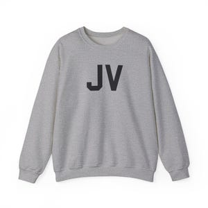 Puede incluir: Una sudadera gris jaspeada con las letras negras "JV" en el centro. La parte superior de manga larga tiene cuello redondo y está hecha de un material suave.