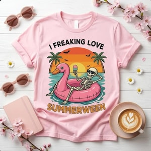 May include: A pink t-shirt featuring the words "I Freaking Love Summerween" and a graphic of a skeleton on a pink flamingo float. The skeleton wears sunglasses and holds an ice cream cone, set against a sunset.