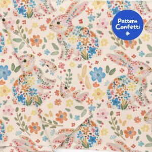 Pode incluir: Um tecido de cor creme claro com um padrão repetitivo de aguarela de coelhos e pequenas flores em tons de laranja, azul, amarelo e verde. Um autocolante circular azul no canto superior direito exibe o texto Pattern Confetti.