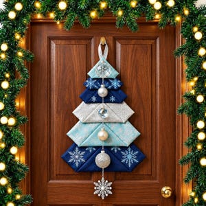 Peut inclure: Une décoration murale en forme de sapin de Noël composée de couches de tissu pliées dans des tons bleu marine, bleu clair et argent. L'arbre présente des motifs de flocons de neige blancs et est orné de boules transparentes, argentées et blanches.