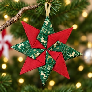 May include: A star-shaped fabric ornament featuring alternating points of solid red cotton and dark green fabric with a gold-colored reindeer and snowflake pattern. The ornament is constructed with folded fabric segments and includes a gold ribbon loop.