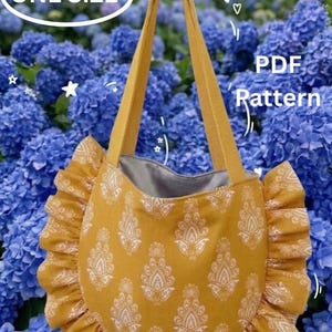 Könnte beinhalten: Eine senfgelbe Tragetasche mit weißem Paisley-Muster, ausgestattet mit einem gerüschten Rand und zwei Schulterriemen. Die Tasche hat ein graues Innenfutter. Der Text auf dem Bild lautet ONE SIZE und PDF Pattern. Die Tasche hängt an einem Haken.