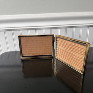 vintage gold-tone metal bi-fold picture frame designed to hold two 5”x 3.5” horizontal photos