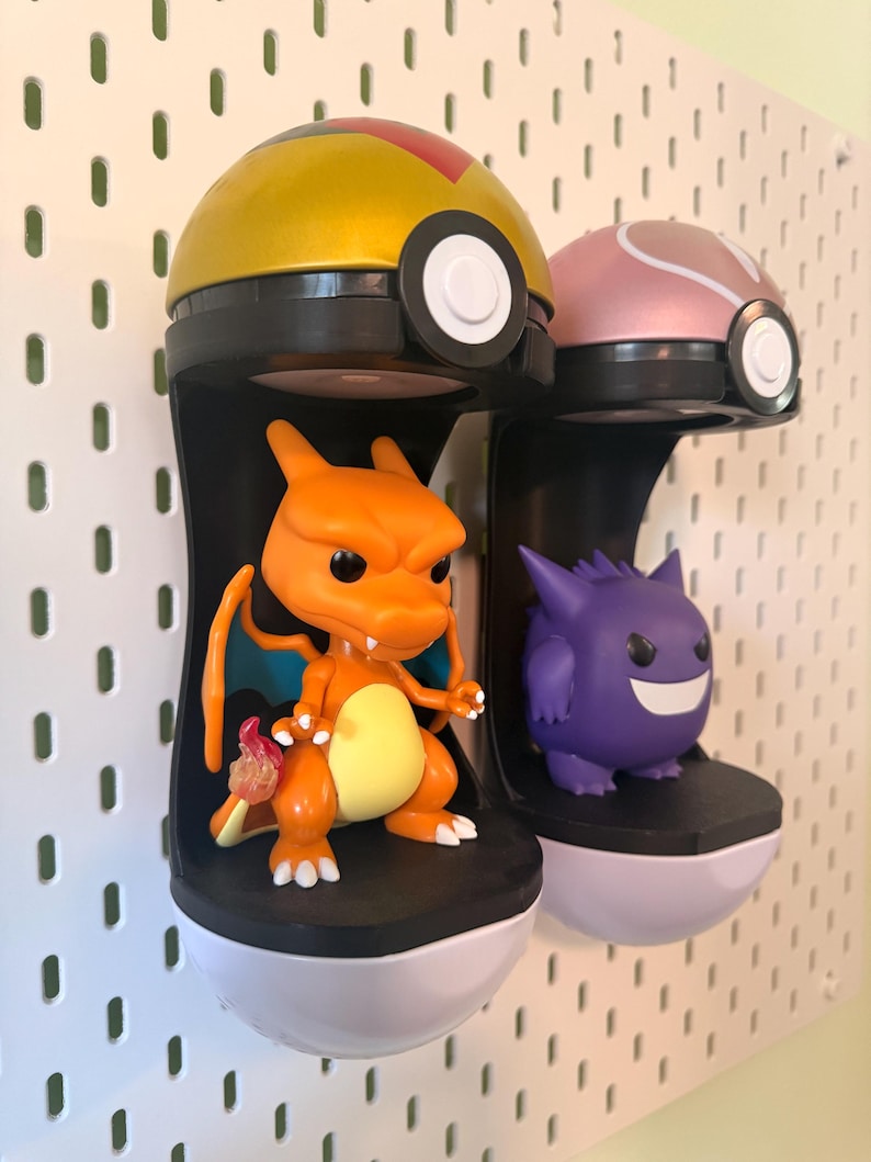 Op de afbeelding: Twee displayrekken met Pok&eacute;mon-thema. E&eacute;n plank bevat een oranje Charizard-figuur en de andere een paarse Gengar-figuur. De planken zijn zwart en wit, met een geel en roze Pokeball-ontwerp erbovenop.