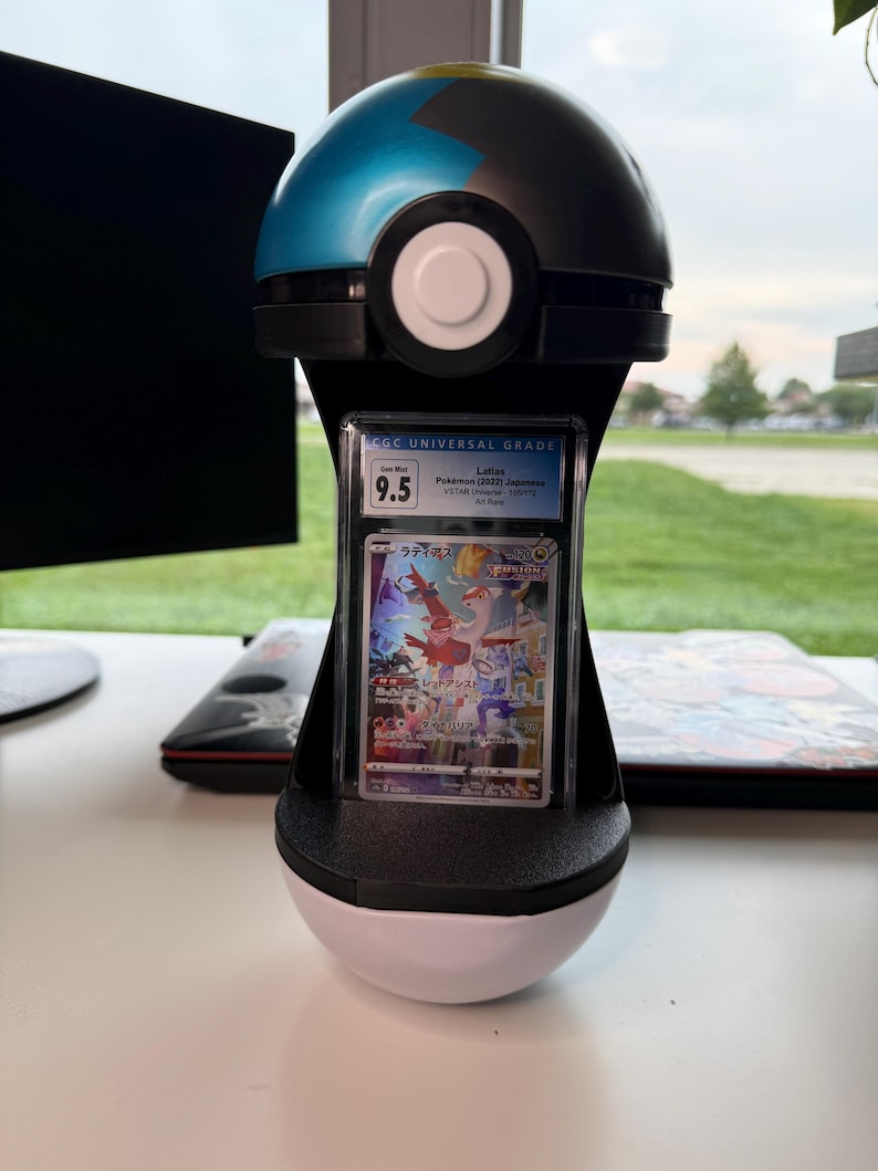 May include: A black and blue spherical display stand shaped like a Poke Ball, holding a vertically oriented, rectangular CGC graded trading card. The card features a Latias illustration with Japanese text and a Gem Mint 9.5 grade label at the top.