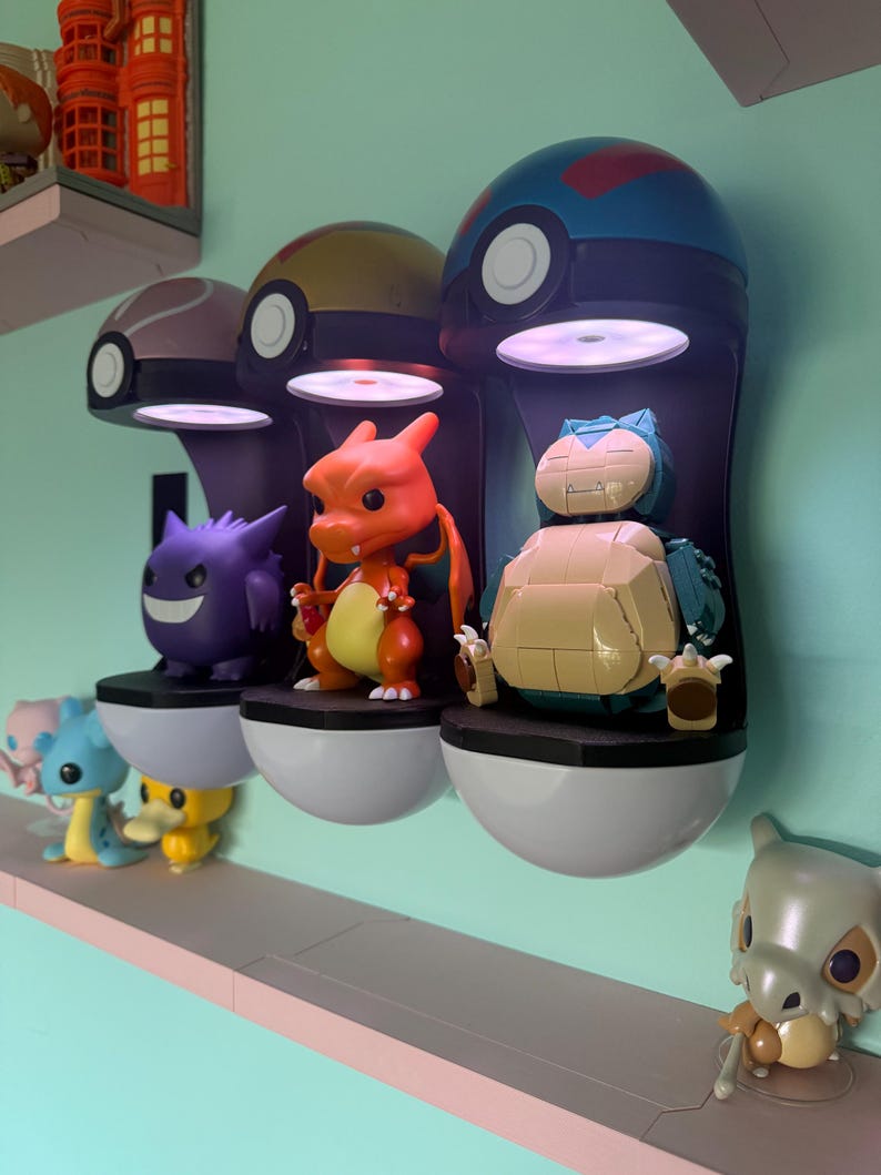 Op de afbeelding: Drie verlichte Pok&eacute;mon-displaykasten, elk met een ander karakterbeeldje. De kasten zijn aan een muur bevestigd, met extra beeldjes op een plank eronder. De kasten zijn zwart met witte en gekleurde accenten.